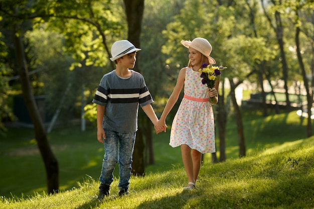 Children's romantic date in summer park, friendship, first love. Boy and girl with bouquet. Kids having fun outdoors, happy childhood