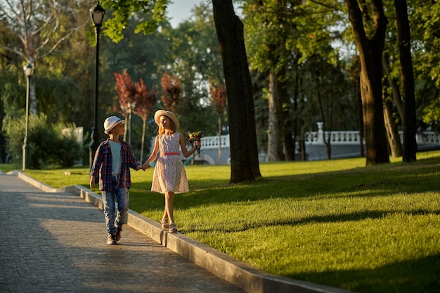 Appuntamento romantico per bambini nel parco estivo, amicizia, primo amore. ragazzo e ragazza con bouquet sul percorso a piedi. bambini che si divertono all'aperto, infanzia felice