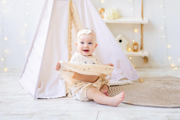 A children's room with a tentwigwam The baby is playing in a cozy bright children's room at home Cozy bright interior for a children's room or a playroom A little girl with toys on a wooden floor