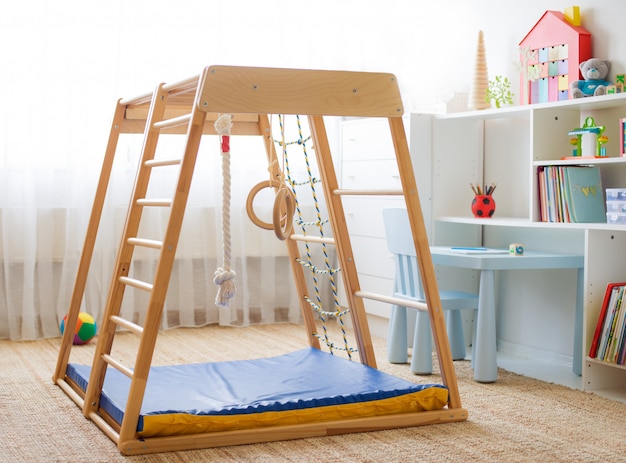 Children's room with a wooden sports complex with stairs, rings and a rope.