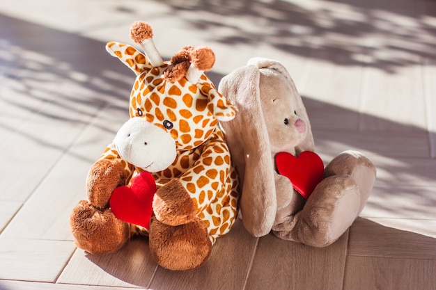 Детская мягкая плюшевая игрушка жираф и кролик сидят на деревянном фоне, жесткий свет и тень