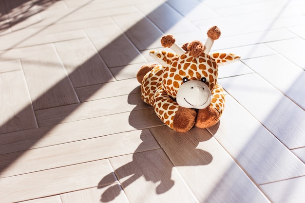 La giraffa morbida del giocattolo della peluche dei bambini si siede su fondo di legno, luce e ombra dure