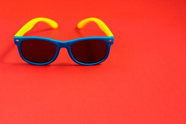 Children's sunglasses on red background. Summer holiday concept, minimalism