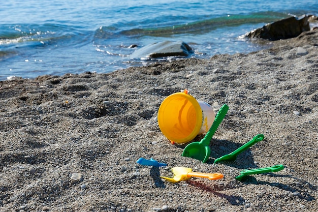 Giocattoli per bambini in riva al mare un secchio una paletta un rastrello giacciono su una spiaggia rocciosa concetto di sicurezza dei bambini