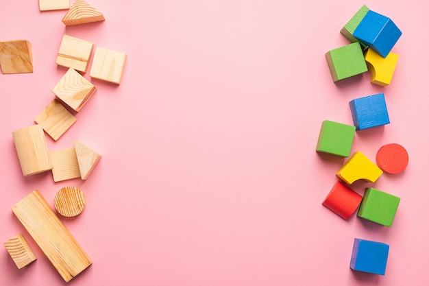 Children's wooden toys on a pink background concept zero west Frame from developing colored cubes Copy space Top view