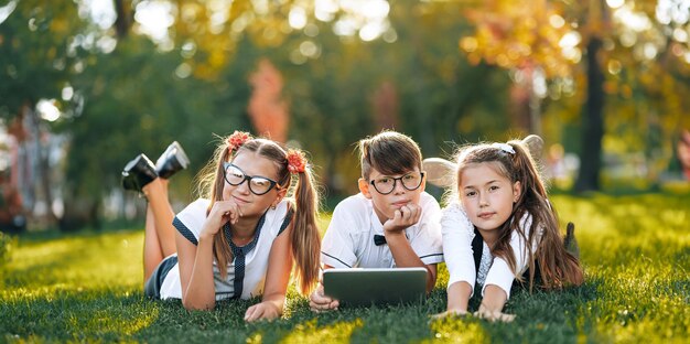 Children schoolchildren are happy near the school on the lawn resting between lessons and studying something on the tablet