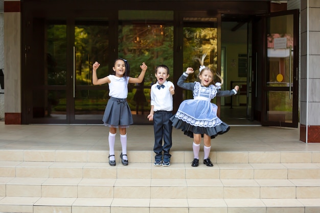 children schoolchildren in school uniforms a boy a blonde girl and a brunette girl jump and rejoicej