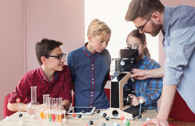 Children and science. Students holding chemistry experiments with teacher in laboratory with liquids, test tubes and flasks. Girl studying samples under the microscope. Stem education, E-learning