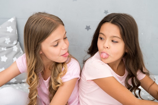 Children show tongue each other. relations sisters or best friends. overcome relations issues. childhood friendship. friends sit back to back show tongues. grimace and emotion. antics showing tongue.