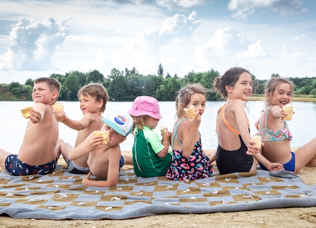 Photo children sit on a blanket by the river and relax after swimming.