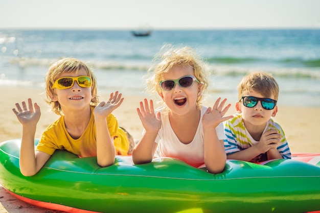 Дети сидят на надувном матрасе в солнцезащитных очках на фоне моря и веселятся
