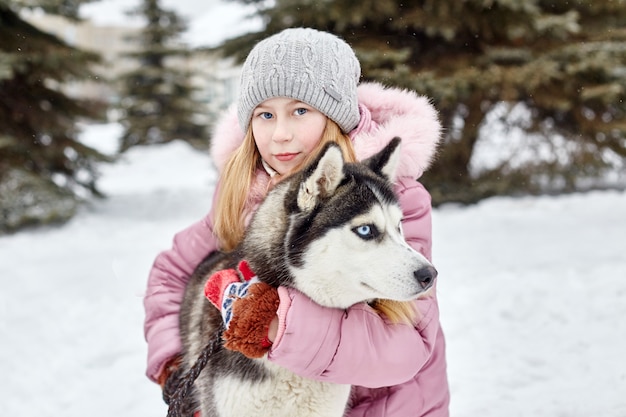 I bambini si siedono sulla neve e accarezzarono il cane husky. i bambini escono e giocano con il cane husky in inverno