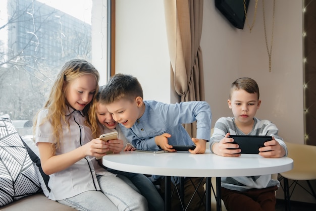 Дети сидят за столиком в кафе и вместе играют в мобильные телефоны. Современное развлечение.