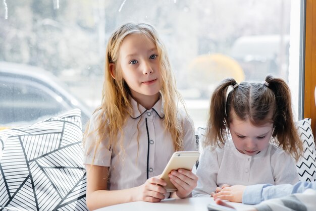 Children sit at a table in a cafe and play mobile phones together.