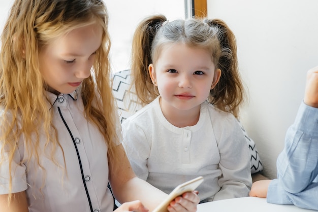 子供たちはカフェのテーブルに座って、一緒に携帯電話を遊びます。