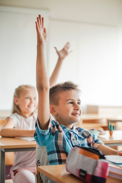 写真 手を上げる学校の机に座っている子供たち