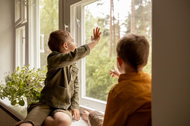 Children sitting on windowsill and waiting for someone comming Two brothers friends Cute preschool kids alone at home Boys are waiting for their mother or father Loneliness Busy parents