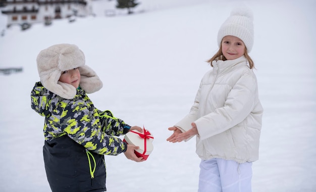 雪の中の子供たち 冬服を着た小さな男の子が小さな女の子にハートの形で贈り物をする