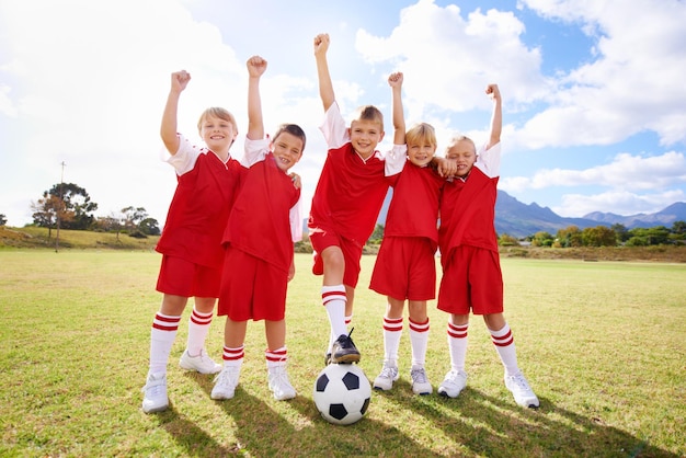 写真 子供のサッカーチームと屋外での勝利または幸せな成功と勝利のお祝い人々の子供たちとフィールドやスポーツでの達成協力とパートナーシップ、またはチームワークのためのガッツポーズ