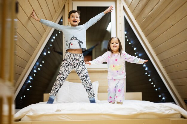 Children in soft warm pajamas playing at wooden cabin home Concept of childhood leisure activity happiness Brother and sister having fun and playing together