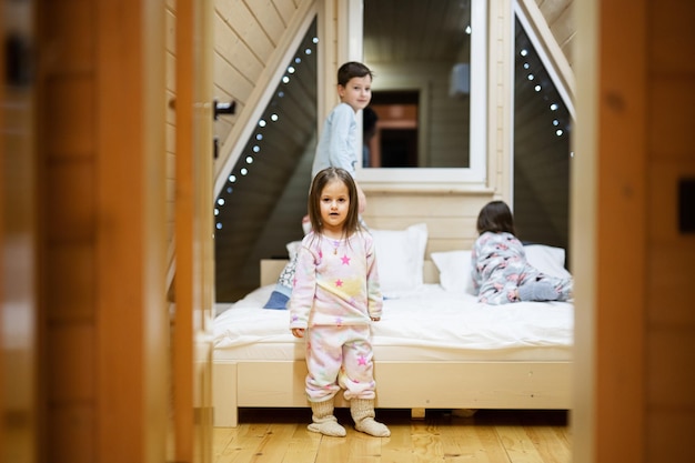 Children in soft warm pajamas playing at wooden cabin home Concept of childhood leisure activity happiness Brother and sisters having fun and playing together