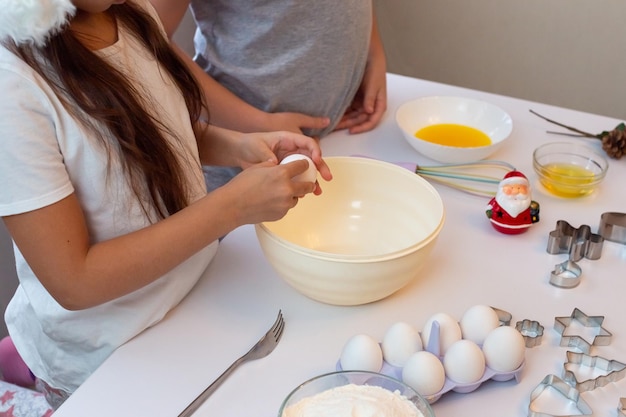 I bambini stanno a un tavolo da cucina bianco preparano i biscotti di natale in cucina