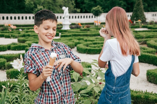 Children teenagers boy and girl are having fun on summer day against background of greenery, eating ice cream together