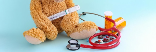 Children toy with thermometer stethoscope and medical pills on blue background increased body