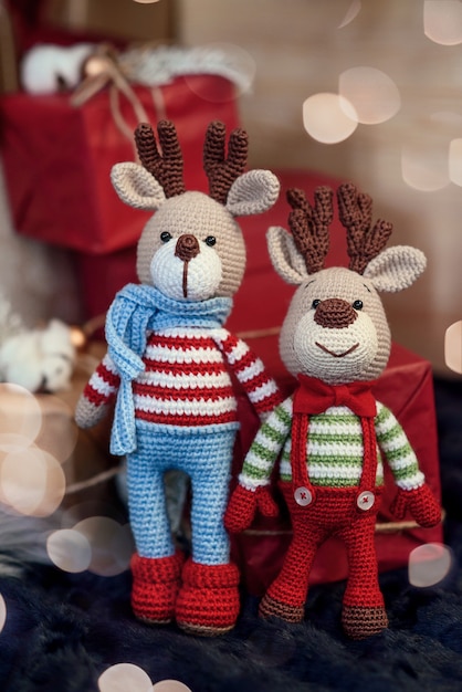 Детские игрушки. Два стильных оленя amigurumi в полосатых свитерах, шарфе и галстуке-бабочке возле рождественских подарков.