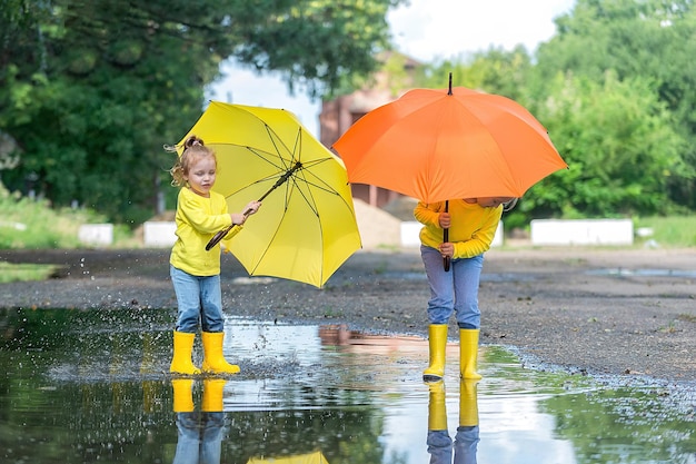 Children two little girls with bright umbrellas in rubber boots
run through the puddles