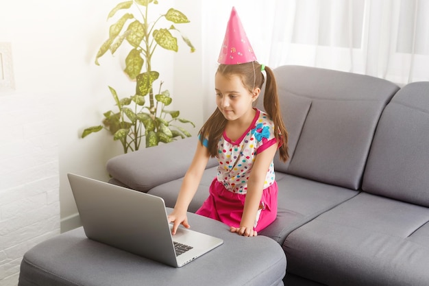 화상 회의에서 친구와 함께 온라인으로 케이크와 함께 어린이 가상 생일 파티. 온라인 회의를 위한 디지털 전화. 격리 시간에 온라인으로 생일을 축하하는 소녀