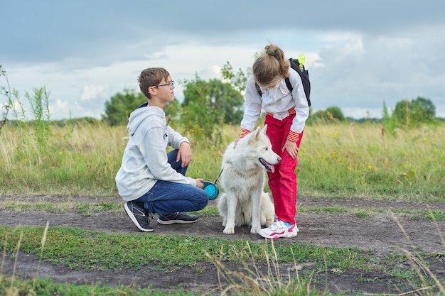 Children walking with white dog in meadow on autumn day