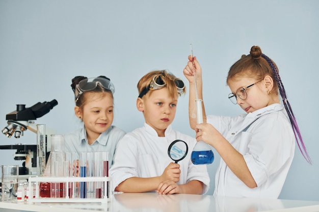 Children in white coats plays a scientists in lab by using equipment