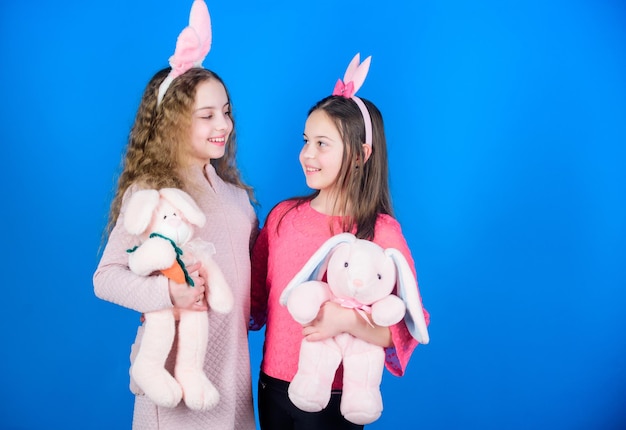 Children with bunny toys on blue background Sisters smiling cute bunny costumes Spread joy and happiness around Friends little girls with bunny ears celebrate Easter Hope love and joyful living