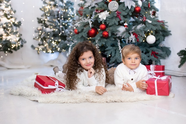 Children with Christmas presents in their hands near Christmas tree and lights