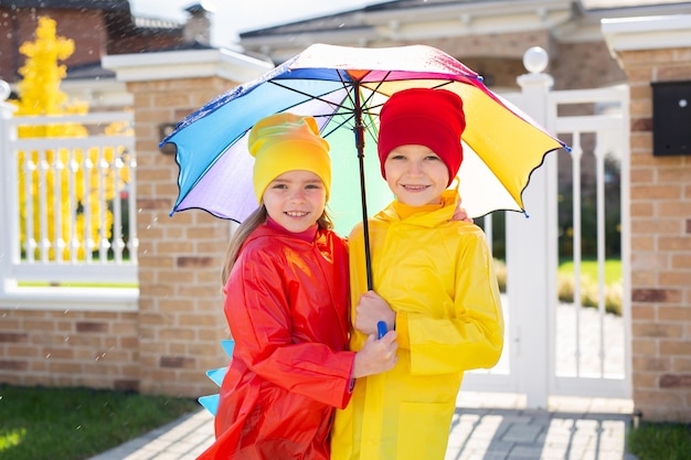 Children with a colorful rainbow umbrella waterproof jacket and coat play in the rain