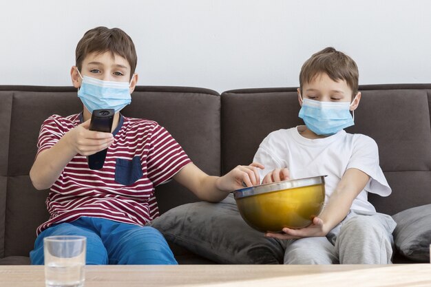 Фото Дети с медицинскими масками смотрят телевизор и едят попкорн