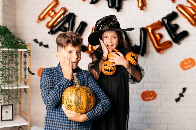 Photo children with pumpkins in their hands against the background of a wall decorated with balloons