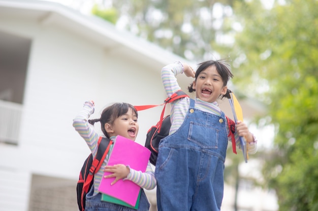 学校の近くの公園でジャンプするリュックサックを持った子供たち。本とバックパックを屋外に持っている生徒