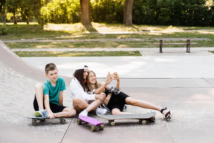 Children with skateboard and penny boards making selfie on phone on the sports playground Children friendship concept Kids smile and laugh and have fun together