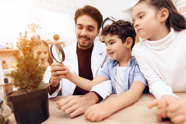 Children with the teacher look through a magnifying glass.