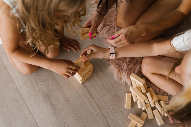 Children with their mother play building a tower of wooden cubes sitting on the floor in the living room Closeup of the arm and the tower