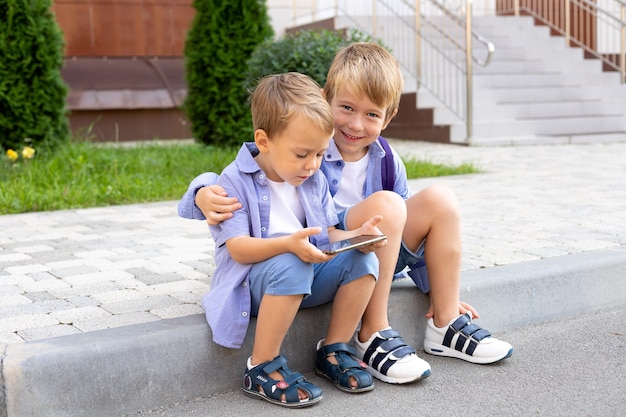 Дети младшего школьного возраста сидят с телефоном возле школы смены в школе