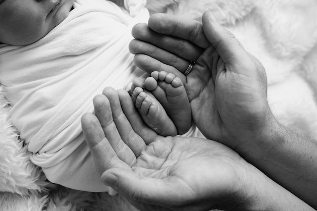 Children39s foot in the hands of mother father parents Feet of a tiny newborn close up Little baby legs Mom and her child Happy family concept Black and white image of motherhood stock photo
