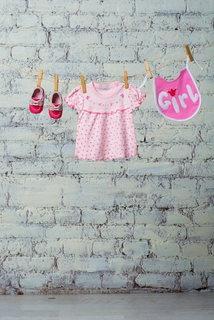 Childrens bib dress and red shoes for the girl dry on a rope on a white brick wall