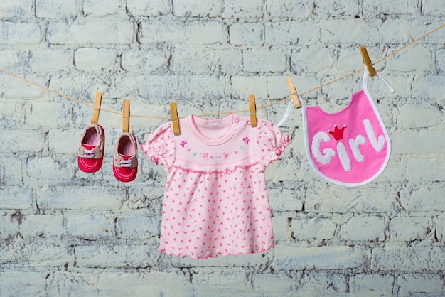 Photo childrens bib dress and red shoes for the girl dry on a rope on a white brick wall