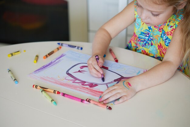 아이들의 창의력. 어린 아이 소녀 집에서 왁 스 연필로 그립니다. 전 세계 검역 기간 동안 온라인으로 원격 학습하는 개념.