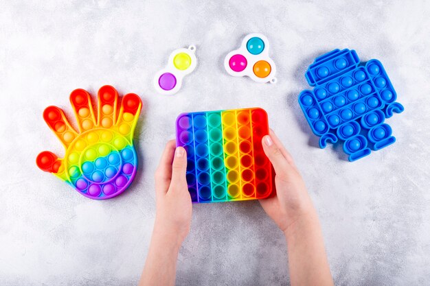 Childrens hand is playing a new trendy silicone toy antistress pop it next to other toys pop it and