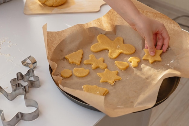 Childrens hand lays dough figurines in the form of christmas symbols on parchment