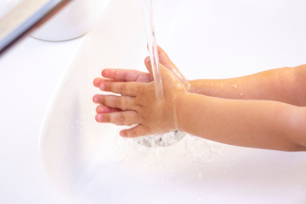 子供の手を洗う。抗菌石鹸の泡で子供の手。細菌、コロナウイルスに対する保護。手指衛生。水で手洗い